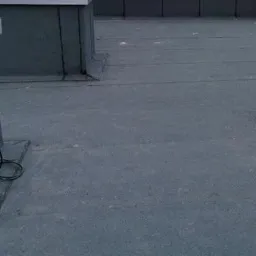 Płaski dach pokryty papą termozgrzewalną z widocznym kablem leżącym na powierzchni, detale obróbek blacharskich przy kominie wentylacyjnym.