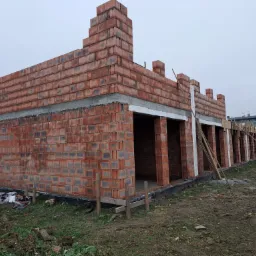 Budowa domu z czerwonej cegły ceramicznej Porotherm, widoczne otwory okienne i drzwiowe, teren budowy z elementami drewna i ziemi.