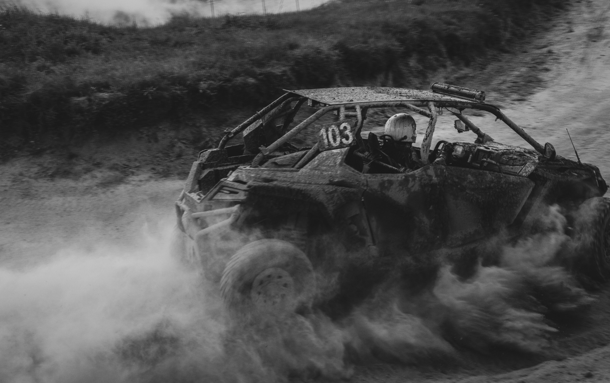 Czarno-białe zdjęcie terenowego pojazdu z numerem 103, pędzącego w chmurze kurzu podczas rajdu.