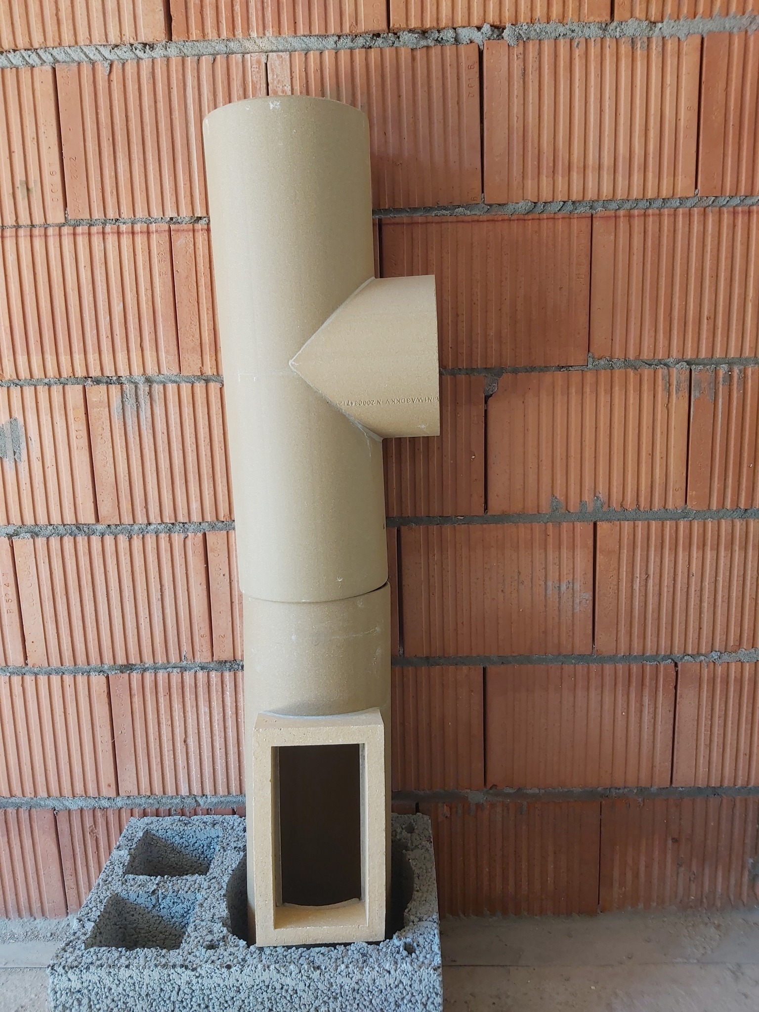 System kominowy z szamotowym wkładem, widoczny na tle ceglanej ściany i betonowego bloczka.