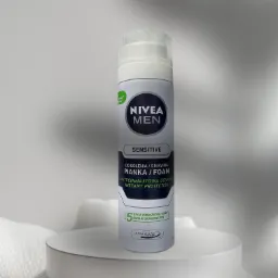 Pionowe ujęcie puszki pianki do golenia Nivea Men Sensitive na białym, okrągłym podeście z ażurowym tłem.