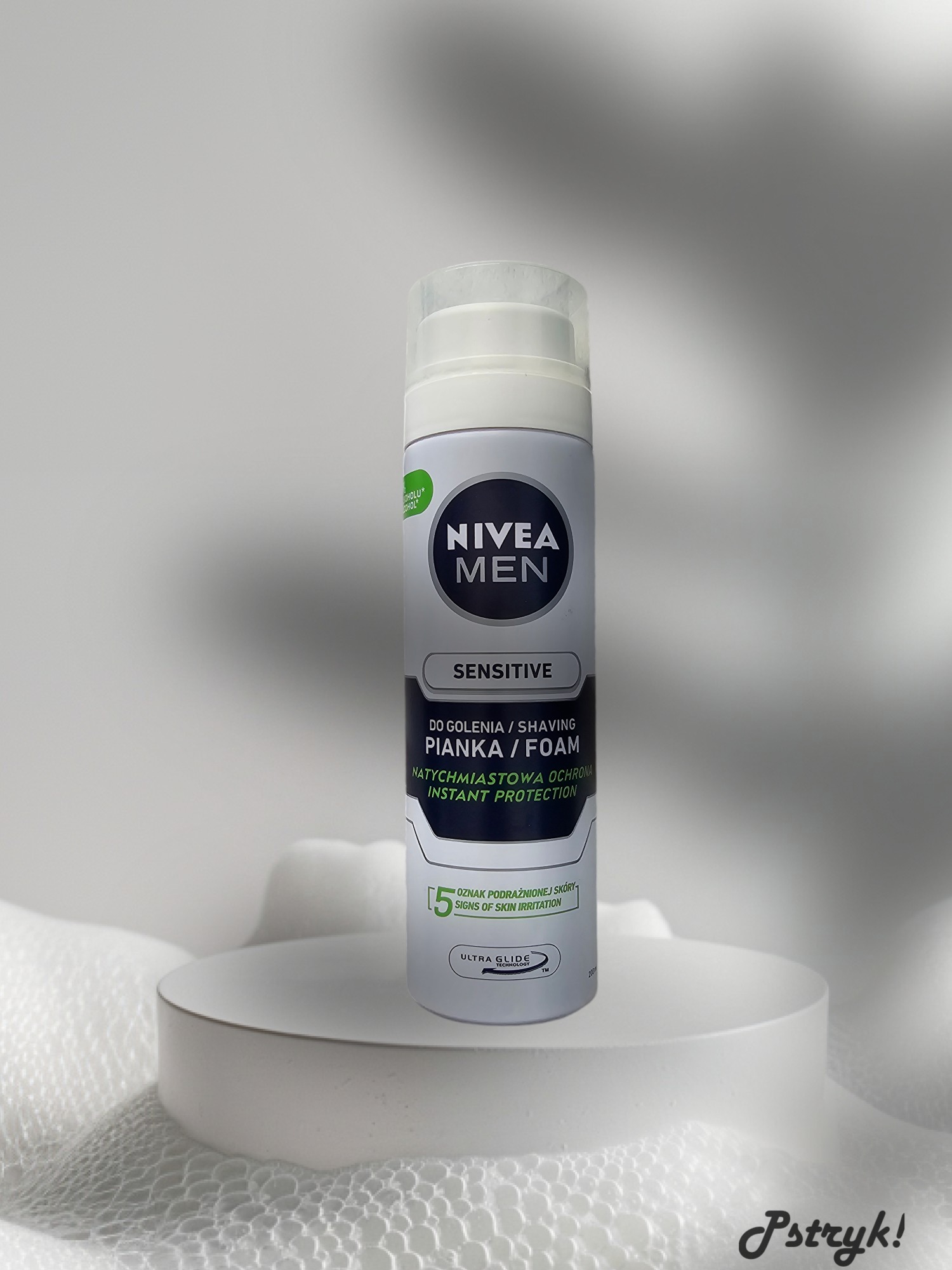 Pionowe ujęcie puszki pianki do golenia Nivea Men Sensitive na białym, okrągłym podeście z ażurowym tłem.