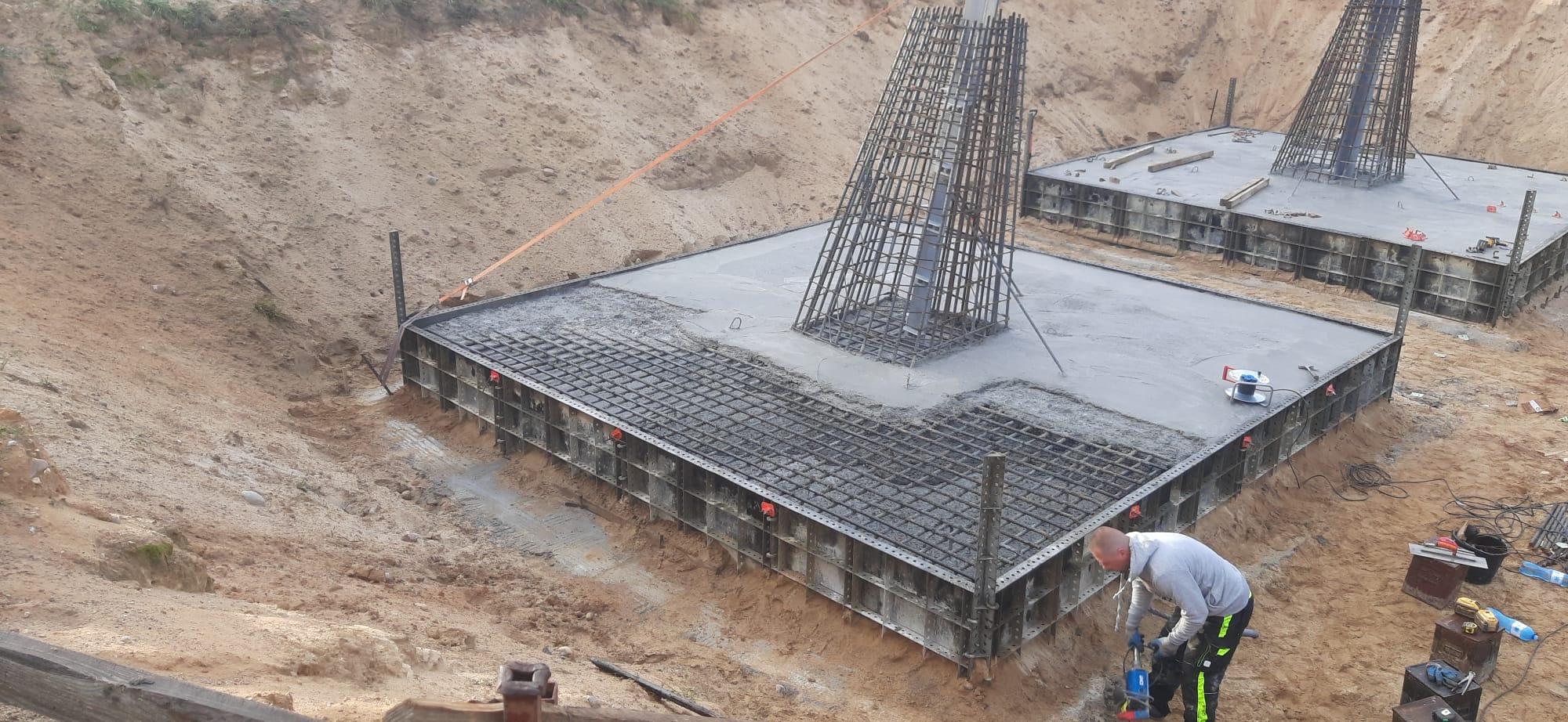 Wylewanie fundamentów pod budynek żelbetowy, widoczny szalunek i zbrojenie, pracownik zagęszcza beton wibratorem wgłębnym, w tle wykop ziemny.