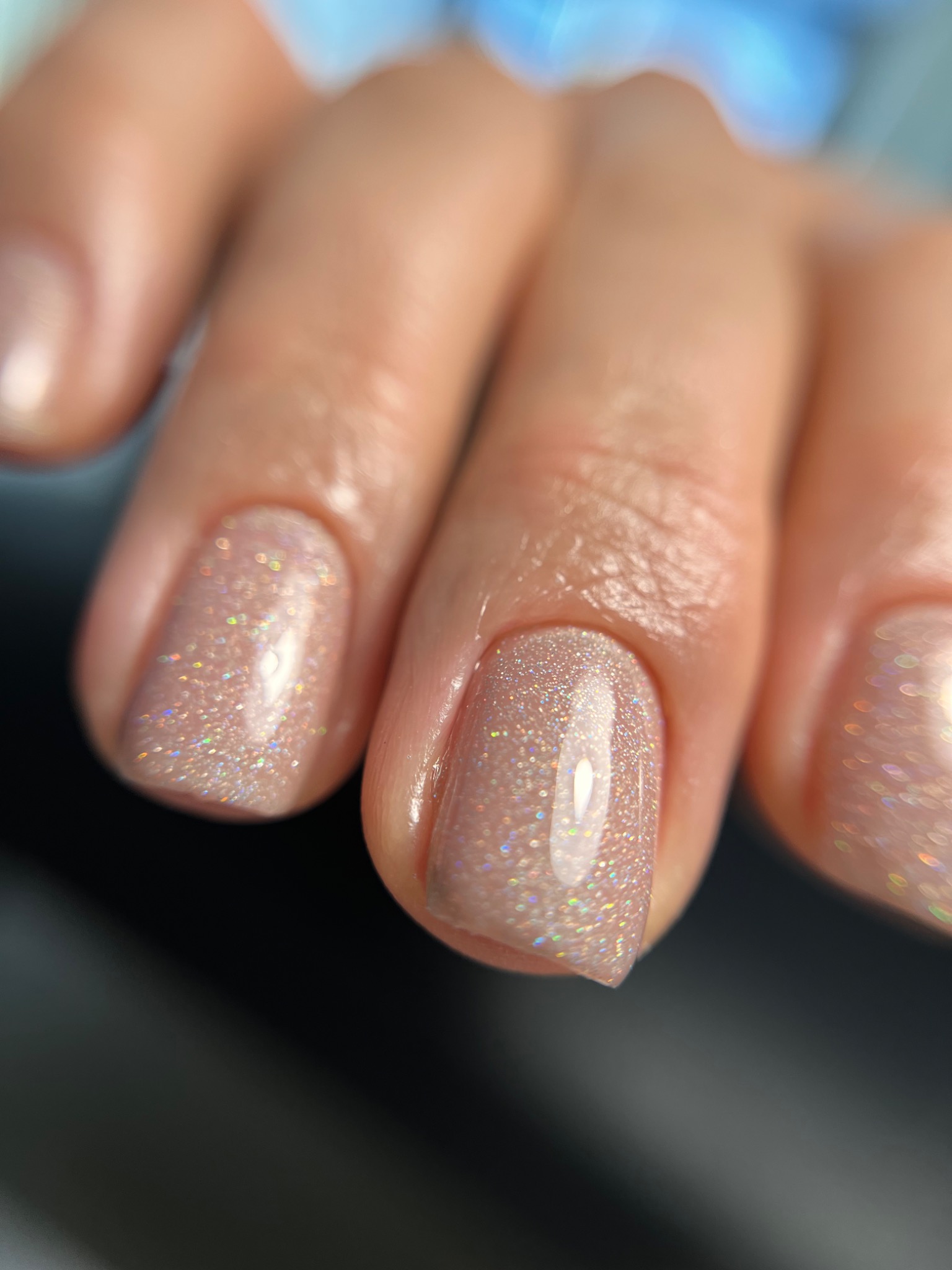 Powiększone ujęcie dłoni z błyszczącym, opalizującym lakierem na paznokciach w odcieniach beżu i różu.