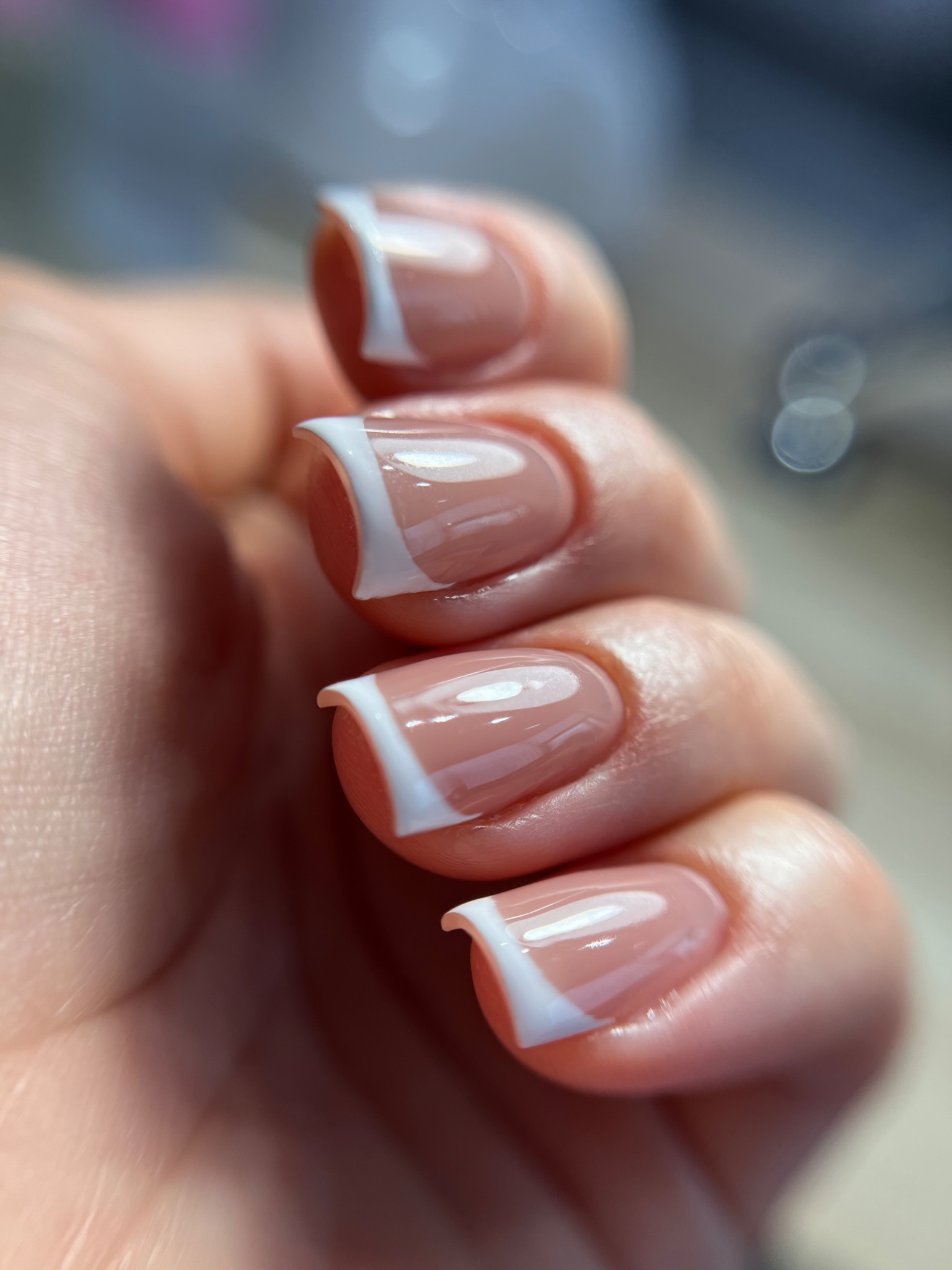 Zbliżenie na dłoń z wykonanym manicure francuskim, gdzie białe końcówki paznokci mają wyraźnie zarysowany, prosty kształt, a całość prezentuje się bardzo schludnie i elegancko.