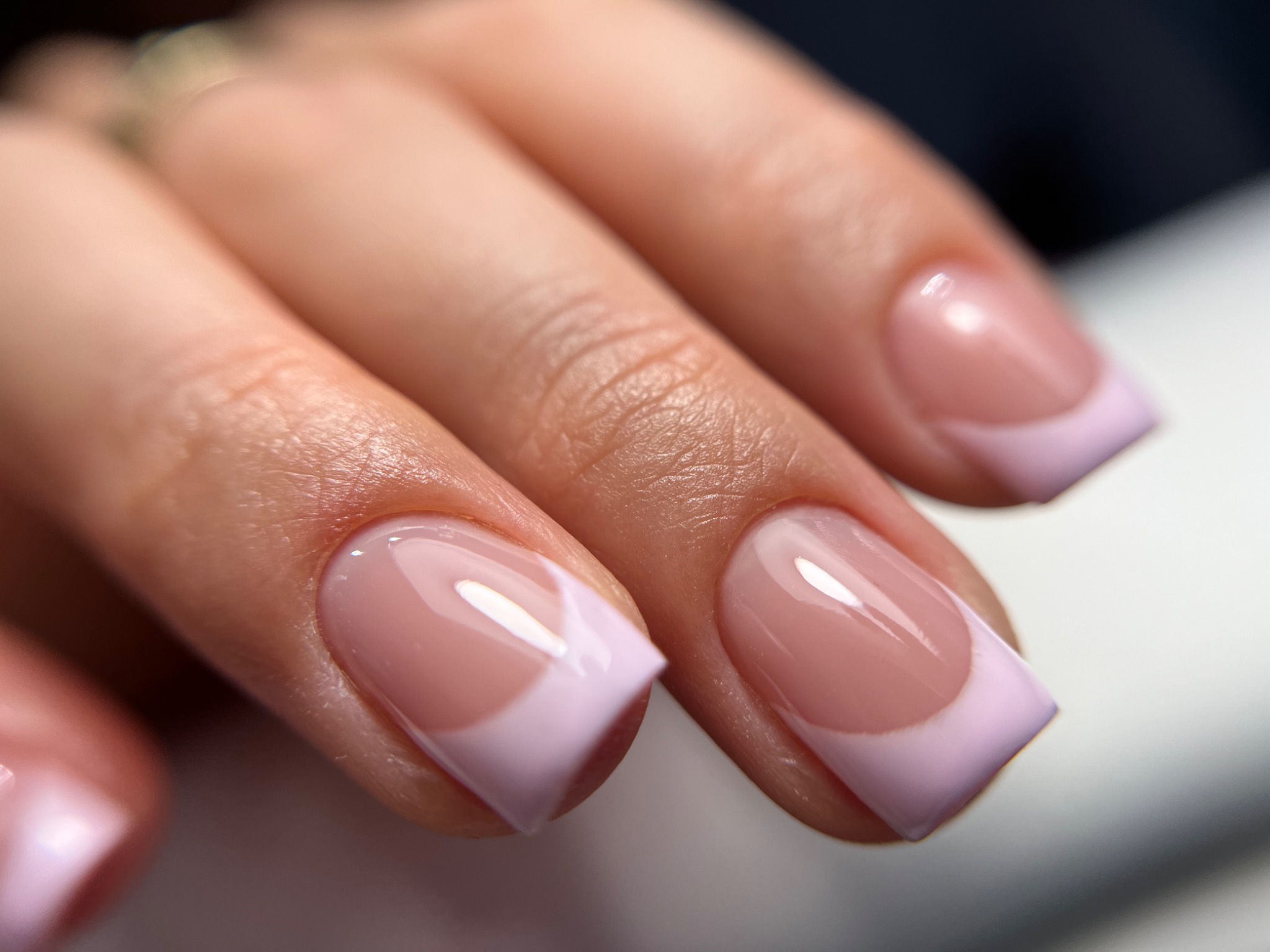 Delikatny french manicure z pastelowym liliowym wykończeniem na kwadratowych paznokciach, zbliżenie na dłoń.