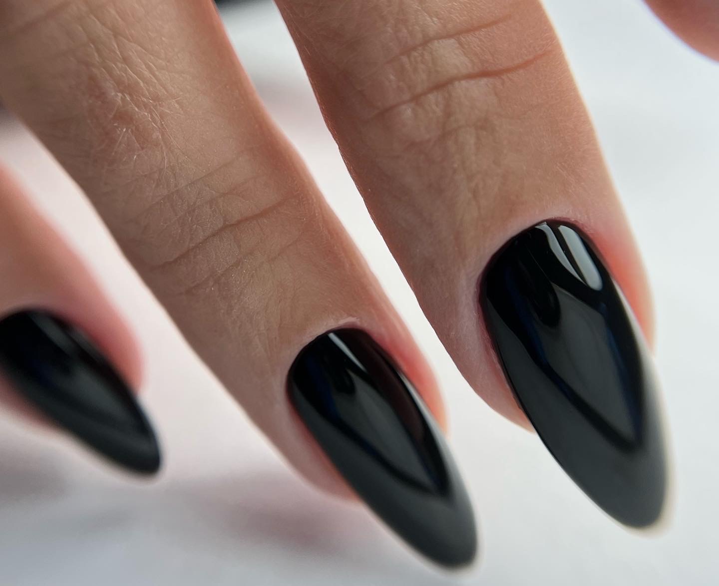 Błyszczące, czarne paznokcie w kształcie migdała na tle jasnej skóry.