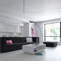 Jasne, przestronne wnętrze z ciemnoszarą sofą narożną, białym stolikiem kawowym i otwartą kuchnią w tle, podkreślone przez minimalistyczne oświetlenie i duże okno z widokiem na zieleń.