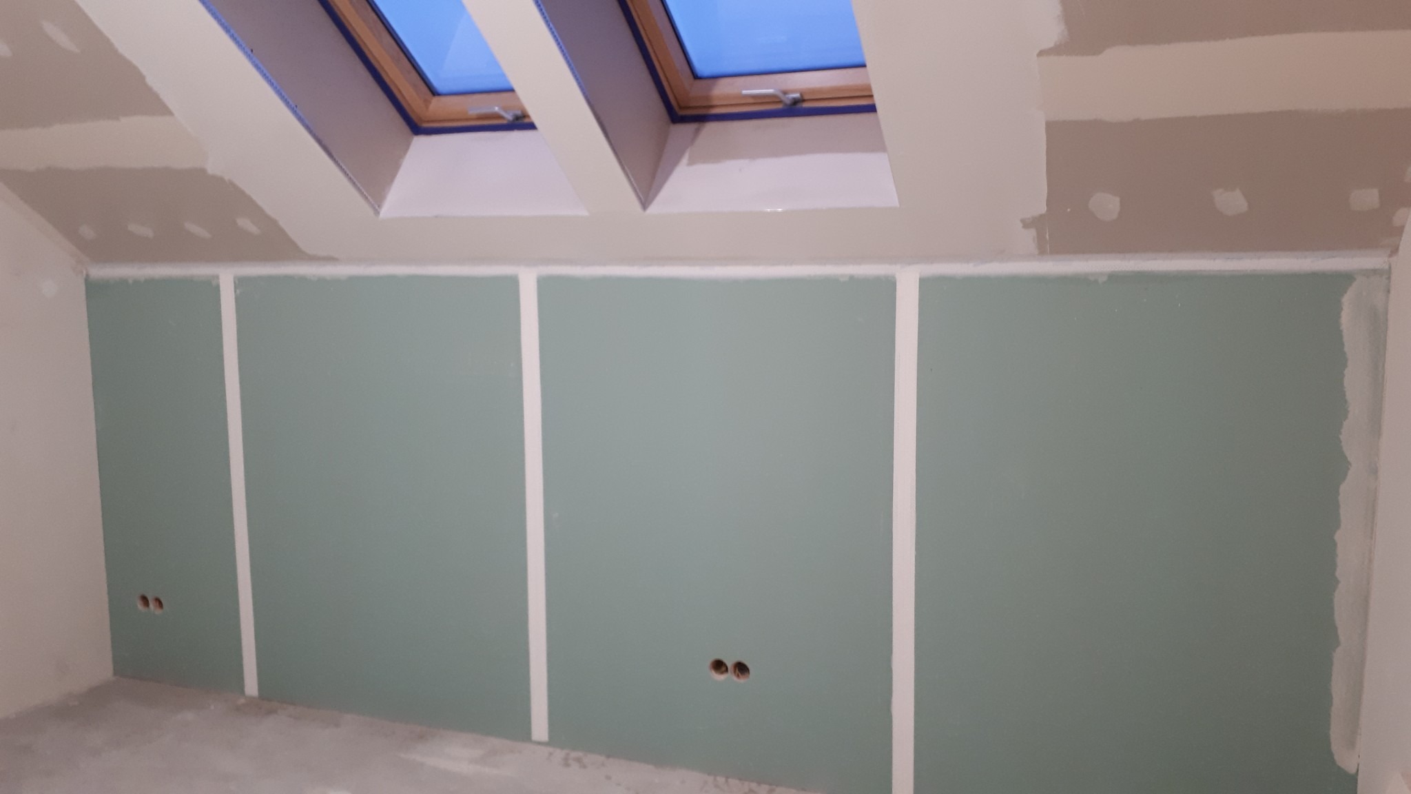 Poddasze z oknami dachowymi i ścianami z płyt gipsowo-kartonowych przed szpachlowaniem, widoczne otwory na gniazdka elektryczne.