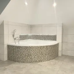 Wykończona łazienka z narożną wanną obudowaną mozaiką w odcieniach szarości i beżu, z jasnymi płytkami na ścianach i podłodze, oświetleniem punktowym w suficie i wnęką z podświetleniem nad wanną.