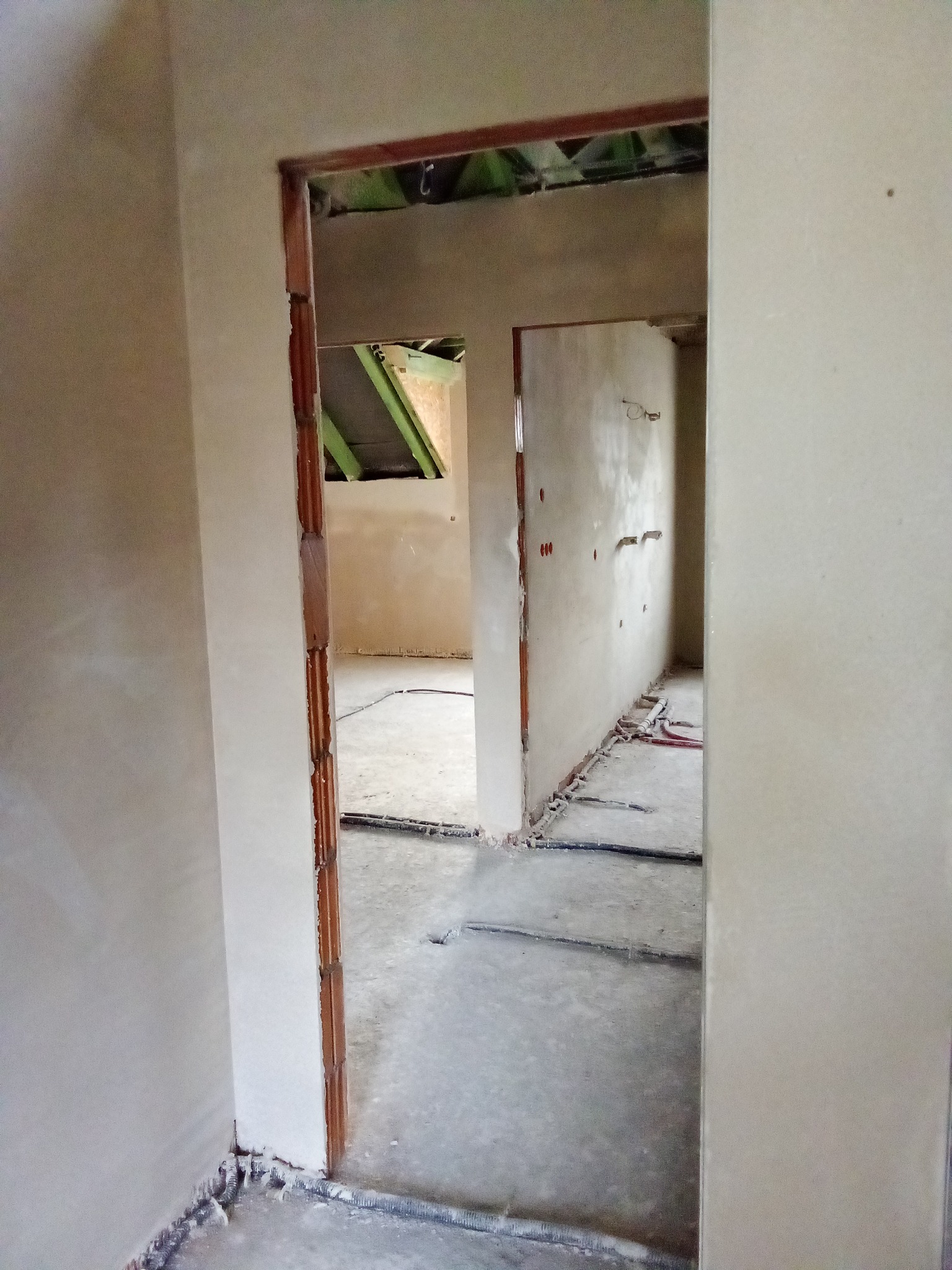 Wnętrze w trakcie prac wykończeniowych: widoczne ściany po nałożeniu gładzi, przygotowane otwory pod instalacje elektryczne oraz fragment surowego stropu z widoczną konstrukcją drewnianą.