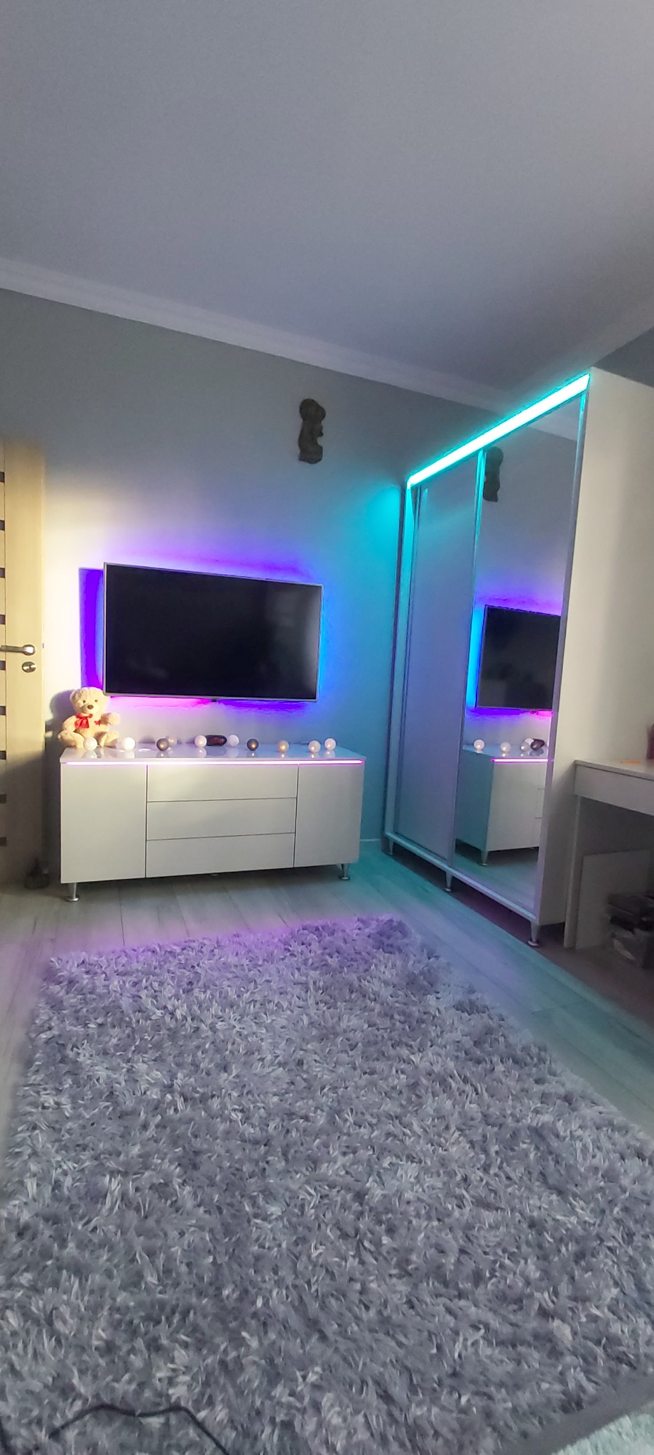 Nowoczesny pokój z szafą wnękową z lustrem i oświetleniem LED, szafką RTV z dekoracjami i puszystym dywanem.