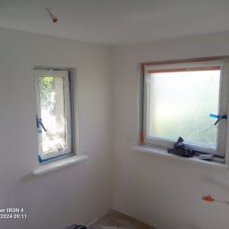 Sławomir kak - Pokój w trakcie malowania: widoczne zabezpieczone okna folią i taśmą malarską, ściany po gładziowaniu, przygotowane do malowania, wystające kable elektryczne.