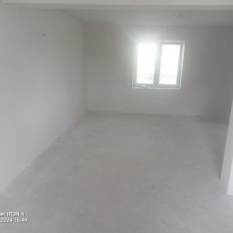 Sławomir kak - Surowe, jasne wnętrze pokoju po wylewce, z widocznymi śladami po pracach budowlanych i okablowaniem pod sufitem, oczekujące na dalsze wykończenie.