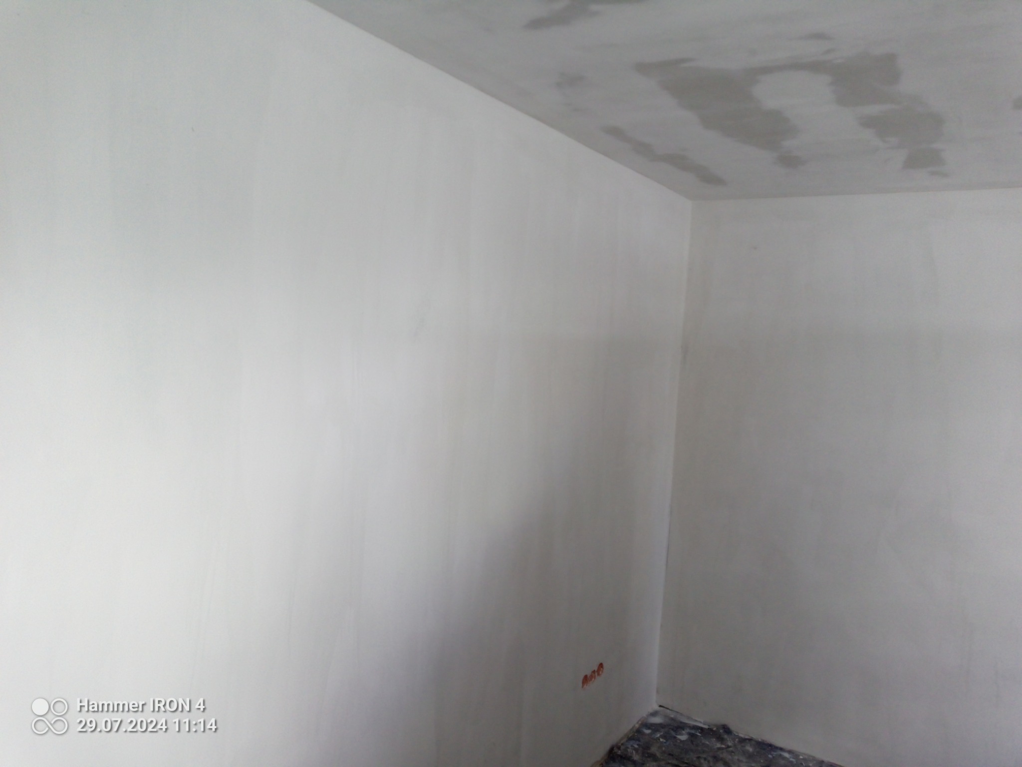 Świeżo wykończone ściany i sufit w rogu pokoju, widoczne ślady po szpachlowaniu na suficie, przygotowane do dalszych prac wykończeniowych.