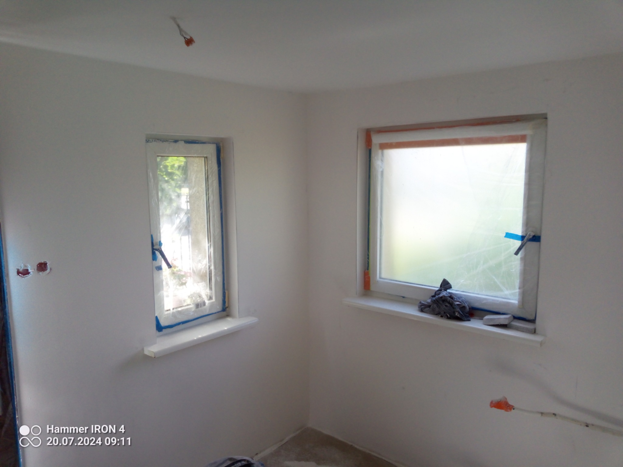 Pokój w trakcie malowania: widoczne zabezpieczone okna folią i taśmą malarską, ściany po gładziowaniu, przygotowane do malowania, wystające kable elektryczne.