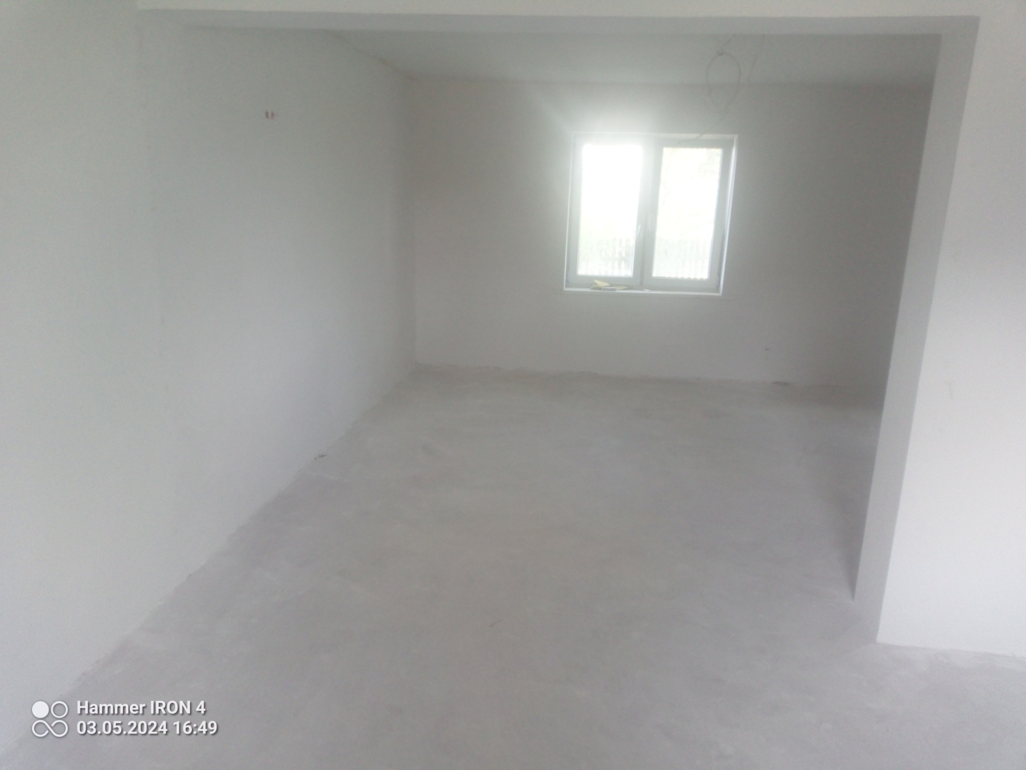 Surowe, jasne wnętrze pokoju po wylewce, z widocznymi śladami po pracach budowlanych i okablowaniem pod sufitem, oczekujące na dalsze wykończenie.