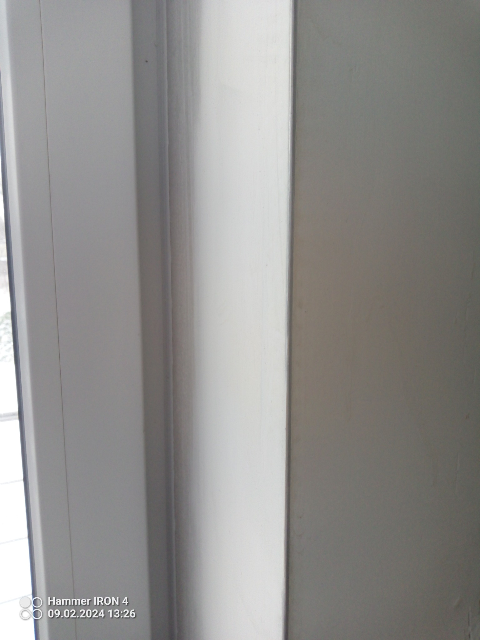 Fragment białej ściany przy oknie z widoczną ramą okienną. Widoczne niedoskonałości w wykończeniu powierzchni ściany.