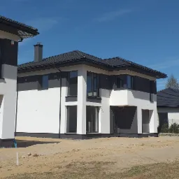 Nowoczesne domy jednorodzinne z ciemną dachówką i białymi elewacjami, widok z poziomu gruntu, bus serwisowy parkuje w pobliżu.