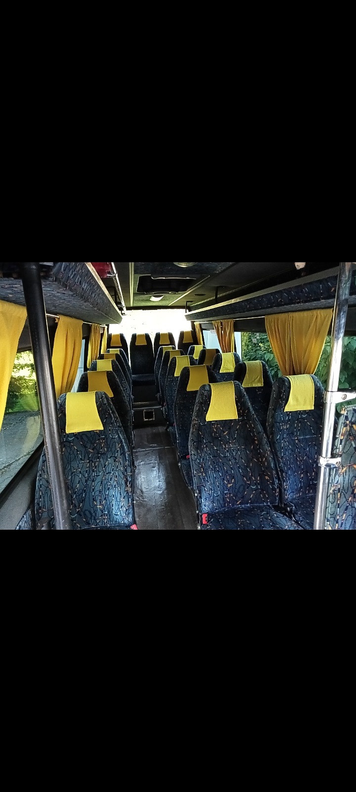 Wnętrze autobusu z rzędami siedzeń w niebiesko-czarne wzory i żółtymi zagłówkami, widok z przodu pojazdu.