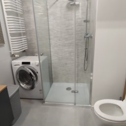 Revo Nieruchomości sp z o o - Nowoczesna łazienka z kabiną prysznicową, pralką Candy, umywalką nablatową i drewnianą zabudową.