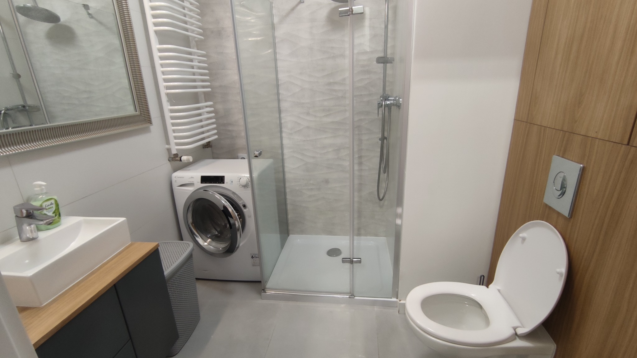 Nowoczesna łazienka z kabiną prysznicową, pralką Candy, umywalką nablatową i drewnianą zabudową.