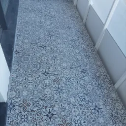 Wzorzyste, ceramiczne płytki podłogowe w odcieniach błękitu, szarości i brązu na balkonie, widoczne białe balustrady i fragment okna.