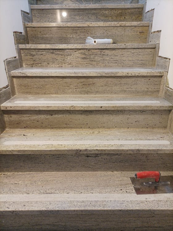 Kamienne schody w trakcie montażu, widoczne narzędzie glazurnicze i rolka folii zabezpieczającej.