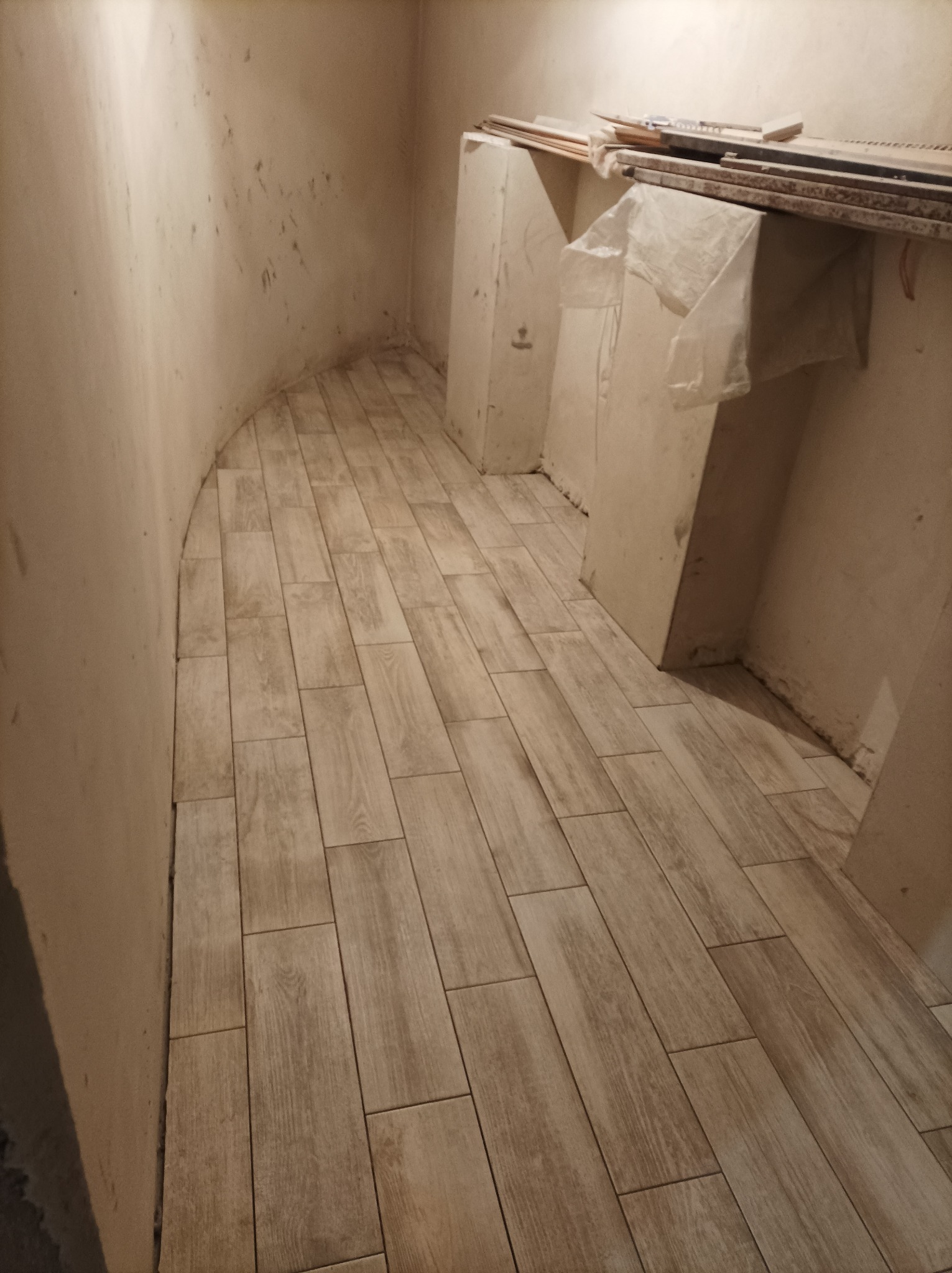 Ułożona podłoga z płytek imitujących drewno w trakcie prac wykończeniowych w pomieszczeniu w Gdańsku. Widoczne surowe ściany i materiały budowlane.