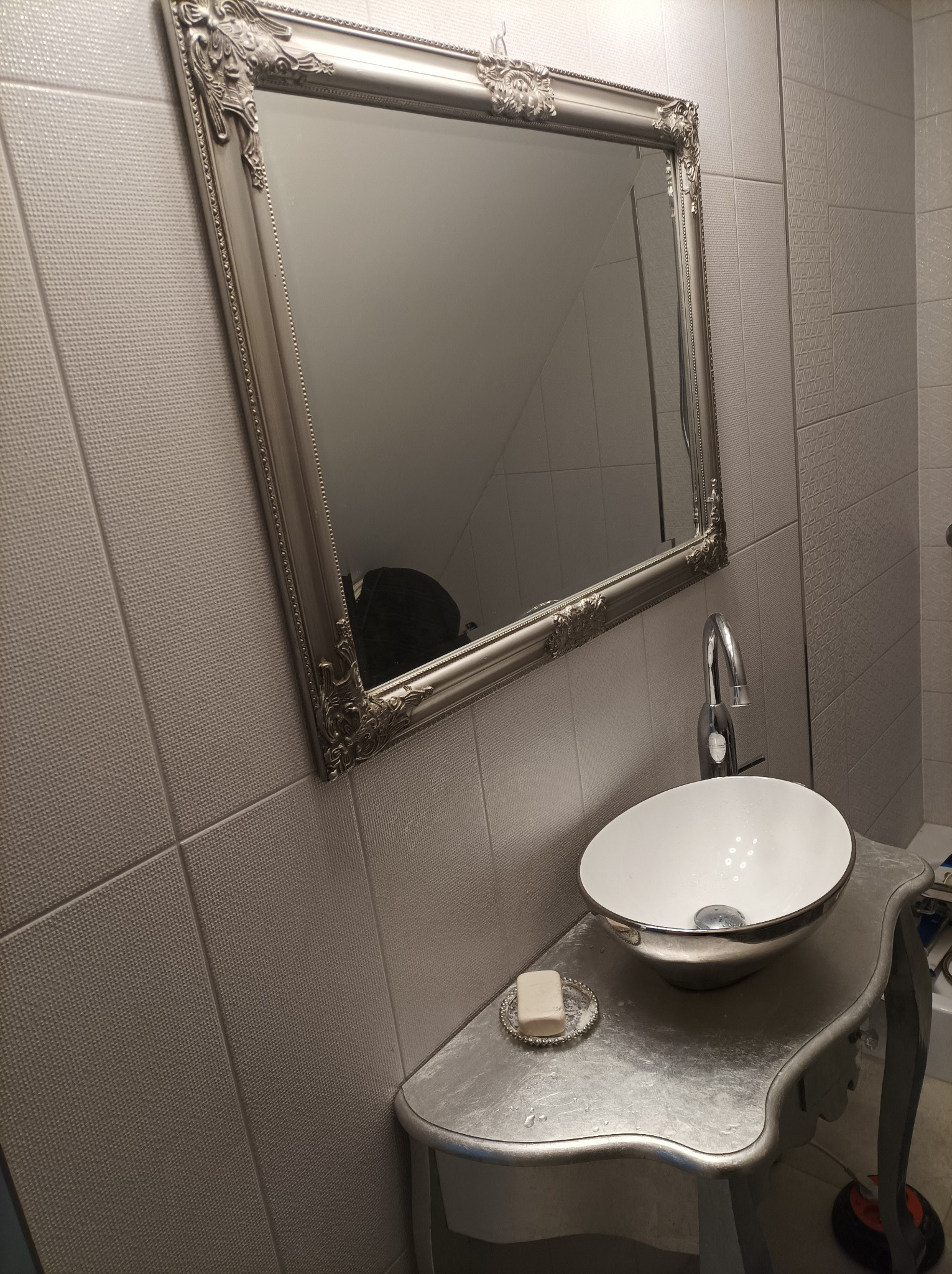 Umywalka nablatowa w stylu glamour z ozdobną srebrną ramą lustra i mydelniczką na blacie, płytki ścienne z subtelnym wzorem.