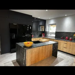 Nowoczesna kuchnia z wyspą: czarne szafki górne, dół w odcieniach drewna, marmurowy blat. Na wyspie misa z owocami, okno w tle. Minimalistyczny design.