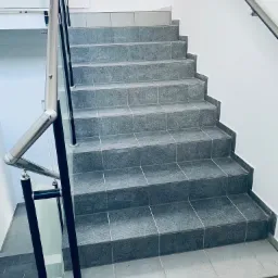 Schody wyłożone szarymi płytkami z metalową balustradą, widok z góry na dół.