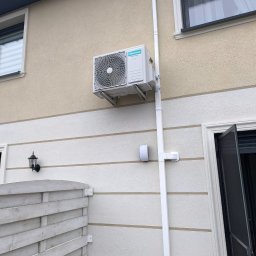 HeatMac Maciej Dobrzyński - Zewnętrzna jednostka klimatyzacji Hisense zamontowana na elewacji domu z widocznymi rurami odprowadzającymi skropliny w białej osłonie.