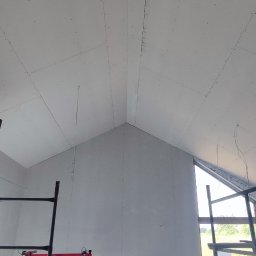ProBud - Montaż płyt gipsowo-kartonowych na skośnym poddaszu, widoczne rusztowania i podnośnik do płyt.