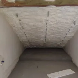 Poddasze po ociepleniu pianką poliuretanową, widoczne metalowe elementy mocujące, ściany w stanie surowym.