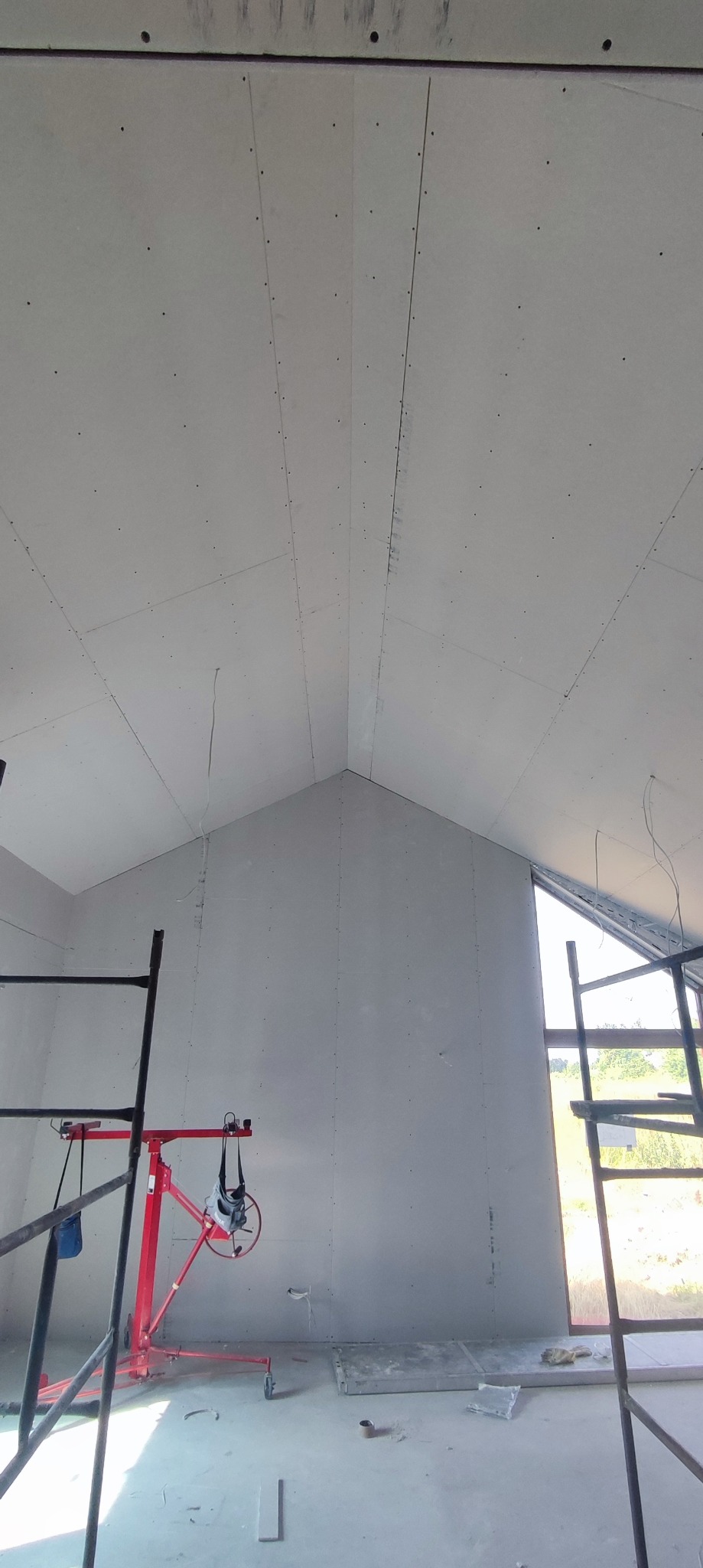 Montaż płyt gipsowo-kartonowych na skośnym poddaszu, widoczne rusztowania i podnośnik do płyt.