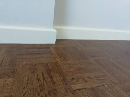 Ułożony parkiet w jodełkę francuską, widok z niskiego kąta, białe listwy przypodłogowe.