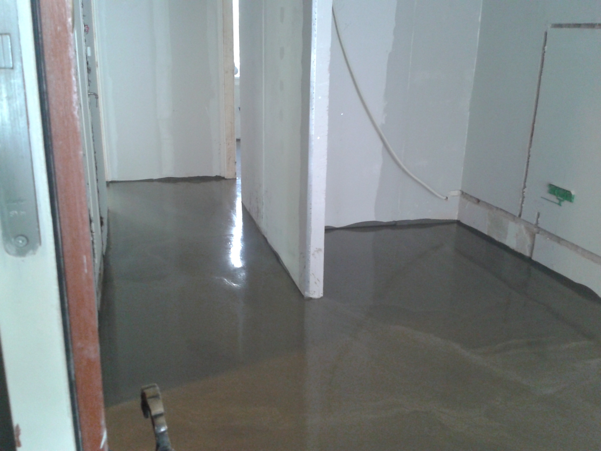 Wylewka samopoziomująca w trakcie schnięcia, widoczne odbicie światła na mokrej powierzchni, ściany przygotowane do dalszych prac wykończeniowych.