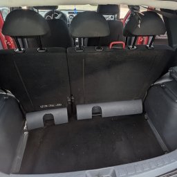 Space Clean - Wnętrze bagażnika czerwonego samochodu z widocznymi elementami tapicerowanymi i wykładziną podłogową, widoczne drobne zabrudzenia.