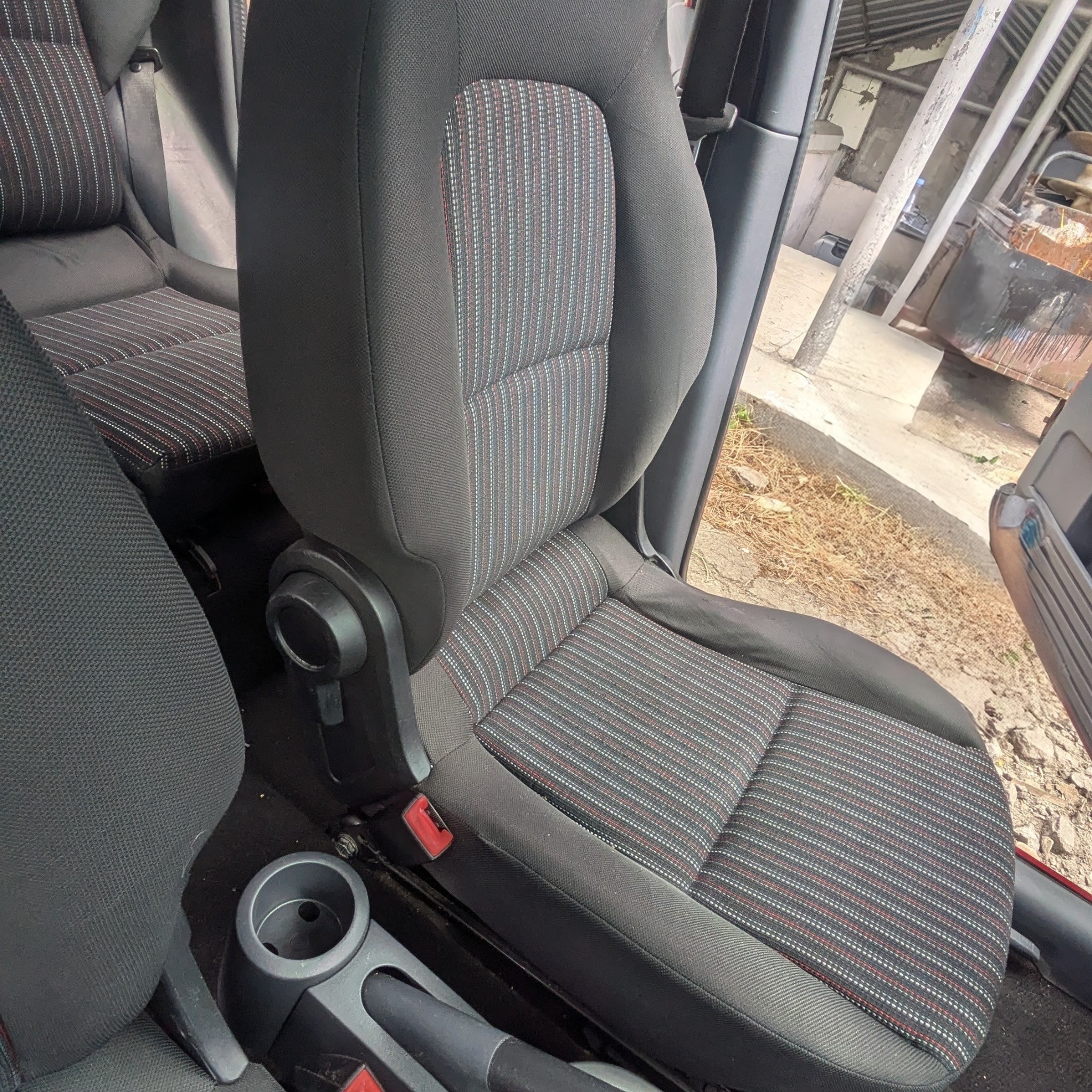 Tapicerowane siedzenie samochodowe z czarną tkaniną i wzorem w paski, widoczne elementy mocowania fotela i fragment wnętrza pojazdu.