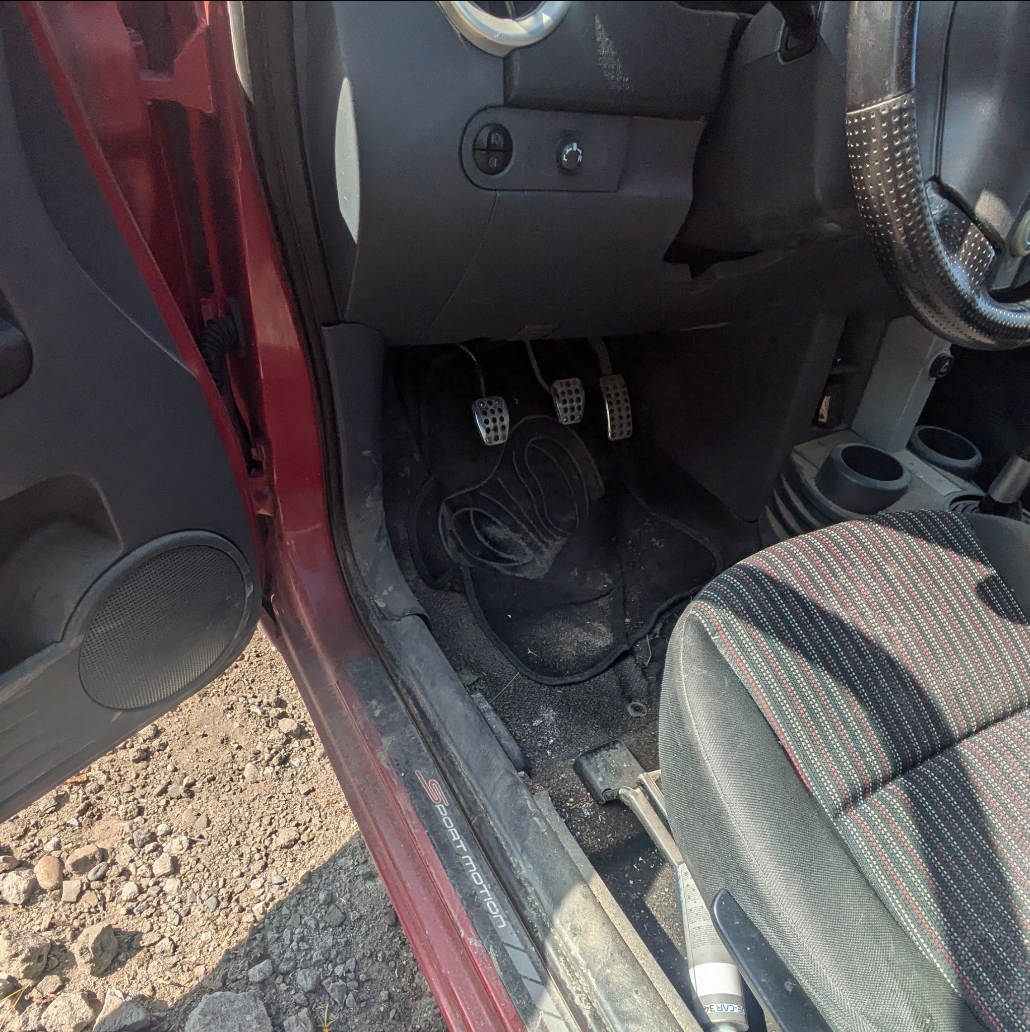 Wnętrze brudnego samochodu w Krakowie, widoczne pedały, dywanik z wyraźnym wzorem i fotel z tapicerką w paski, wymagające odświeżenia.