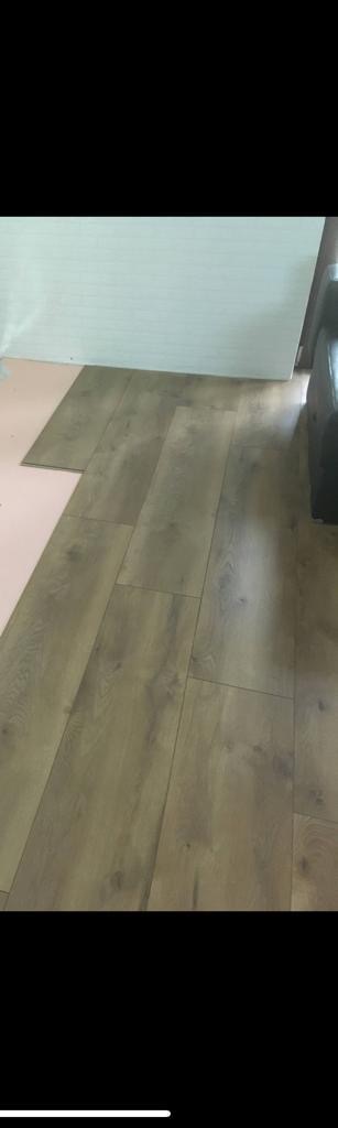 Fragment podłogi w trakcie układania paneli laminowanych, widoczna warstwa izolacyjna z różowej pianki pod niezakończonym fragmentem podłogi.