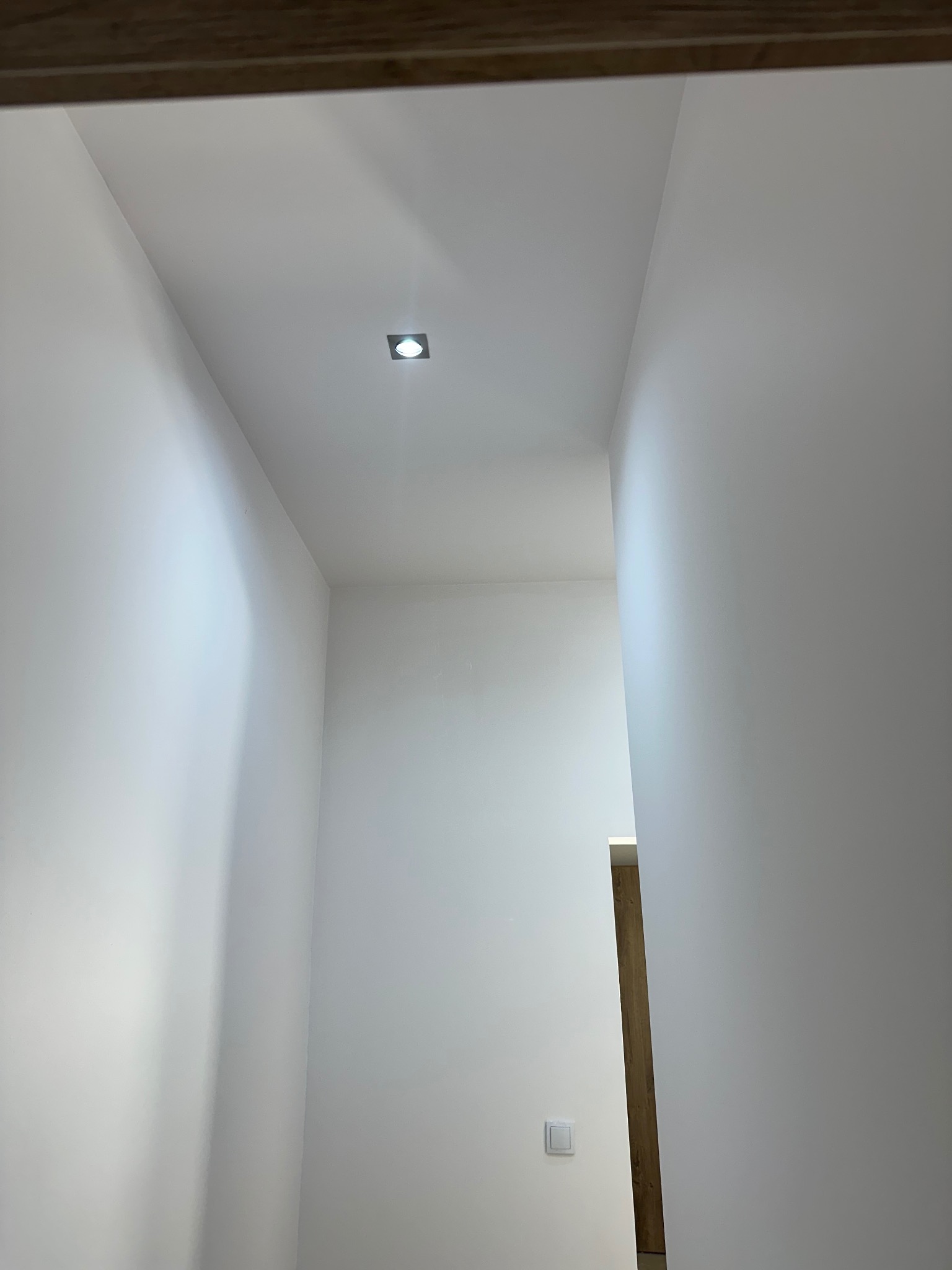 Białe ściany korytarza po malowaniu z wbudowanym oświetleniem punktowym i włącznikiem światła. Widok z dołu.