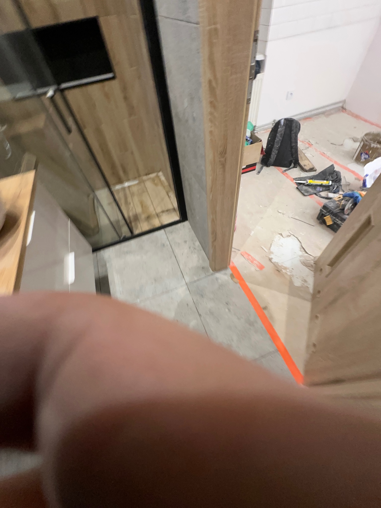 Remont łazienki w trakcie: widoczna kabina prysznicowa z drewnopodobnymi panelami, szare płytki podłogowe i narzędzia na podłodze. Ujęcie z bliska, zamazane.