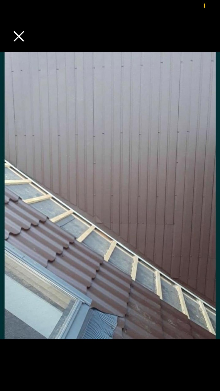 Brązowe blaszane pokrycie dachowe w trakcie montażu, widoczne łaty drewniane i fragment okna dachowego.