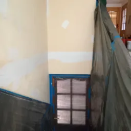 Przygotowanie ścian do malowania: ściany zabezpieczone folią i taśmą malarską, widoczne fragmenty nałożonej gładzi.