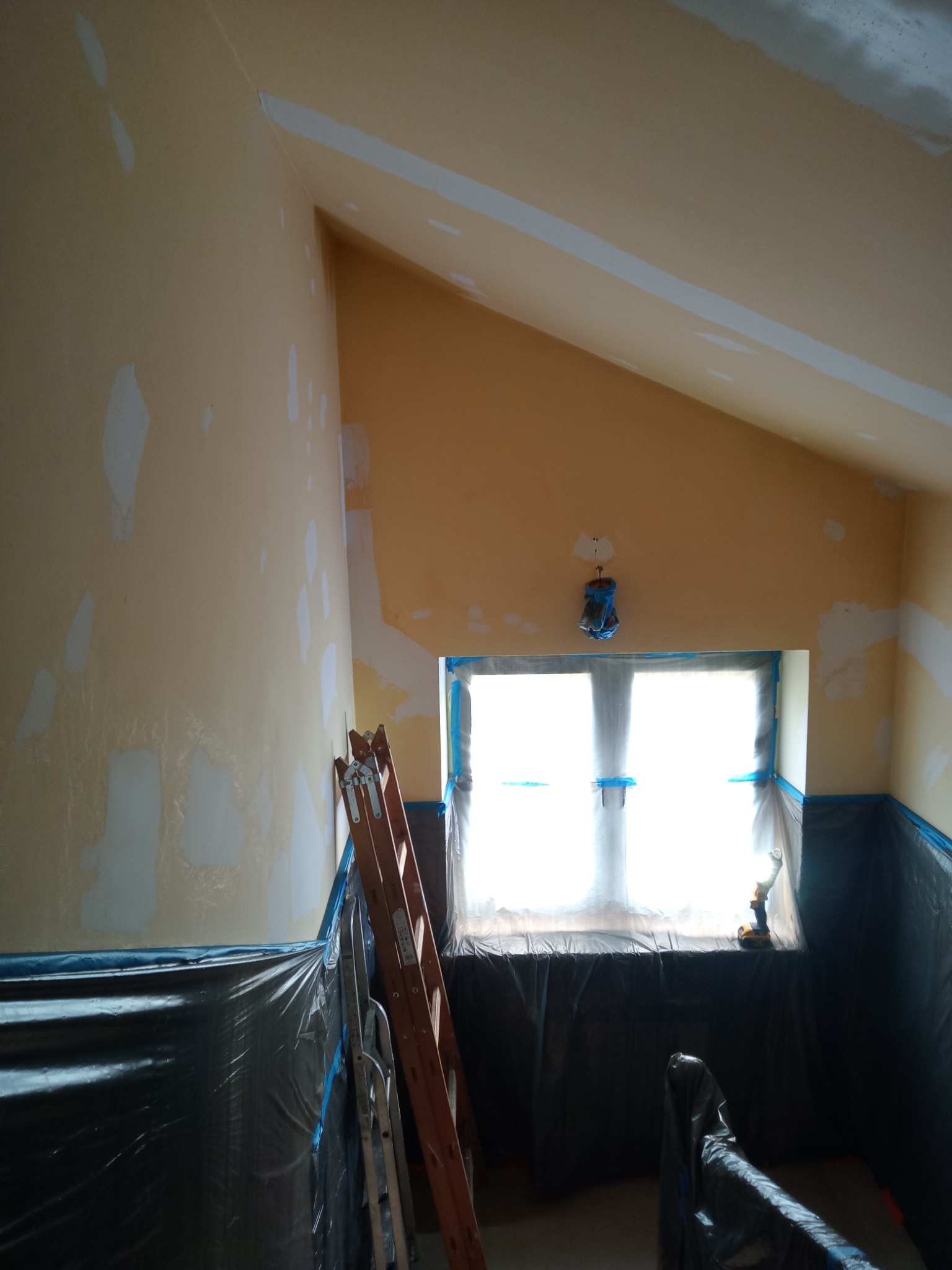 Pokój na poddaszu w trakcie remontu: ściany przygotowane pod gładzie, częściowo pokryte łatami, okno zabezpieczone folią, drabina oparta o ścianę.