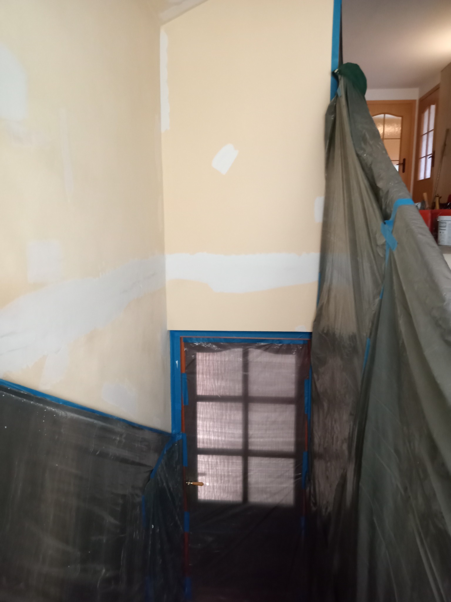 Przygotowanie ścian do malowania: ściany zabezpieczone folią i taśmą malarską, widoczne fragmenty nałożonej gładzi.