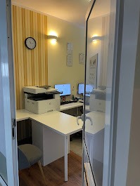 Jasne biuro rachunkowe z dwoma stanowiskami komputerowymi, drukarką na białym biurku i zegarem na ścianie z tapetą w pionowe pasy, widok zza otwartych drzwi.