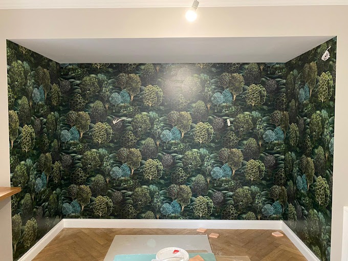 Pokój wytapetowany tapetą z motywem leśnym, widoczne niedoskonałości przy podłodze i suficie, na podłodze zabezpieczenia z kartonu.